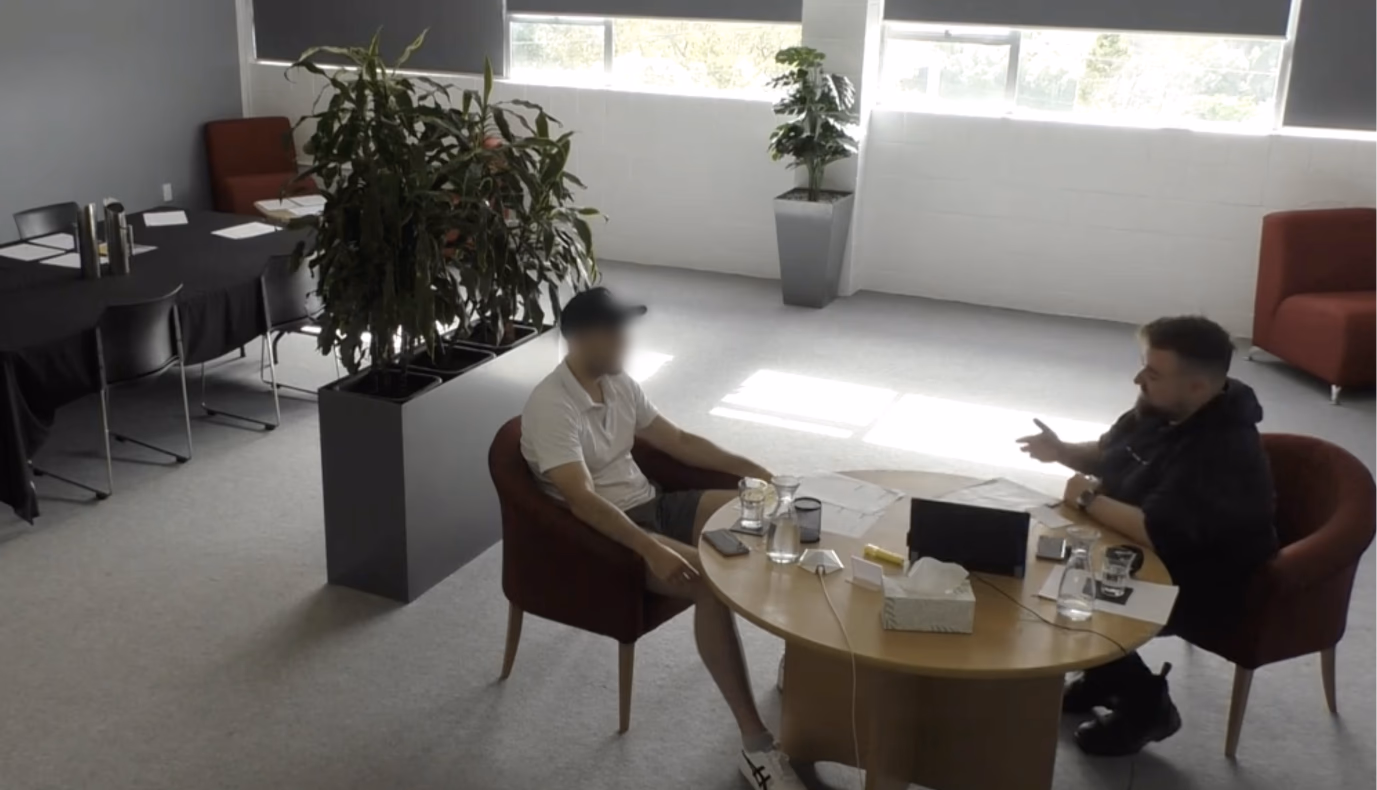 Ein runder Tisch, an dem zwei Männer einander gegenübersitzen und miteinander sprechen.